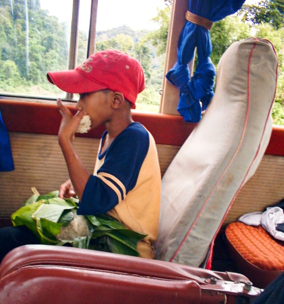 バスの座席に座ってもち米を食べているラオスの少年の写真