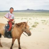 ７～８歳くらいの少年が馬にのっている写真。モンゴルの草原