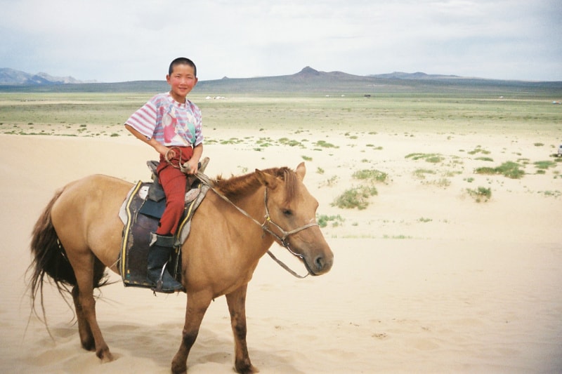 ７～８歳くらいの少年が馬にのっている写真。モンゴルの草原