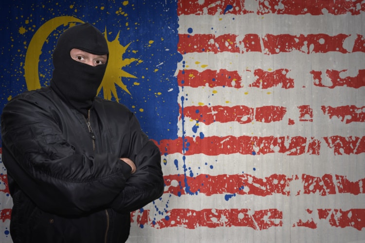 マレーシア国旗の前にマスクのあやしい男が腕組みして立っている写真