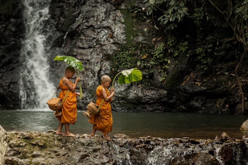 ルアンパバーン。6歳～8歳くらいの少年僧侶が大きな葉っぱを持って水際を歩いている写真