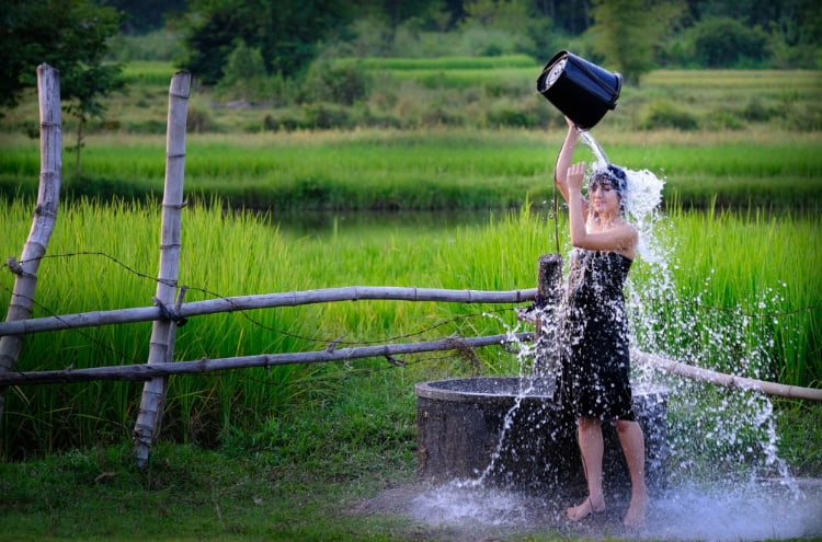 女性がバケツで井戸水を浴びている写真