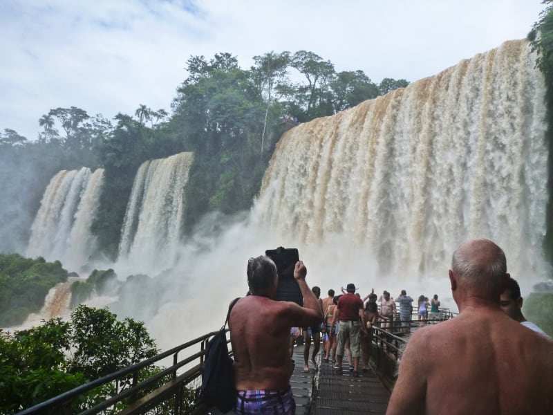 巨大の滝のまえに人がたくさん。上半身裸の男性も数名いる写真