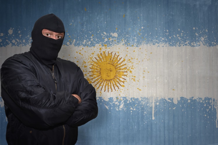 アルゼンチン国旗の前にマスクの男が立っている