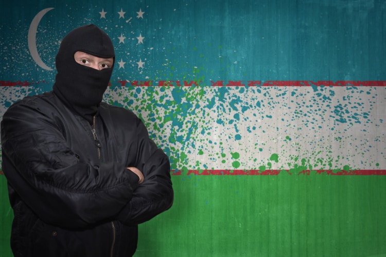 ウズベキスタン国旗の前にマスクの怪しい男が立っている