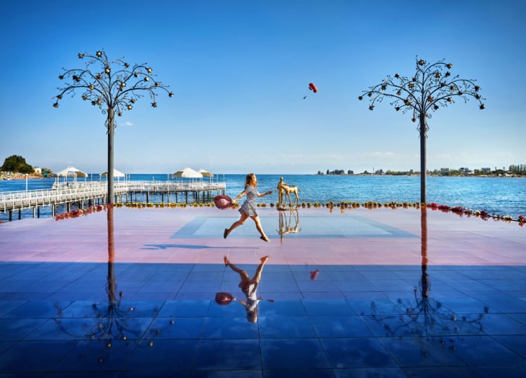 イシク・クル湖の桟橋の前で女性が楽しそうに歩いている。女性の像が水面にも映っている