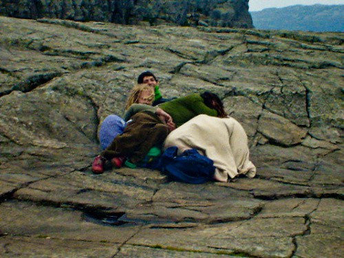 崖の地面の上で毛布にくるまった男女が四人