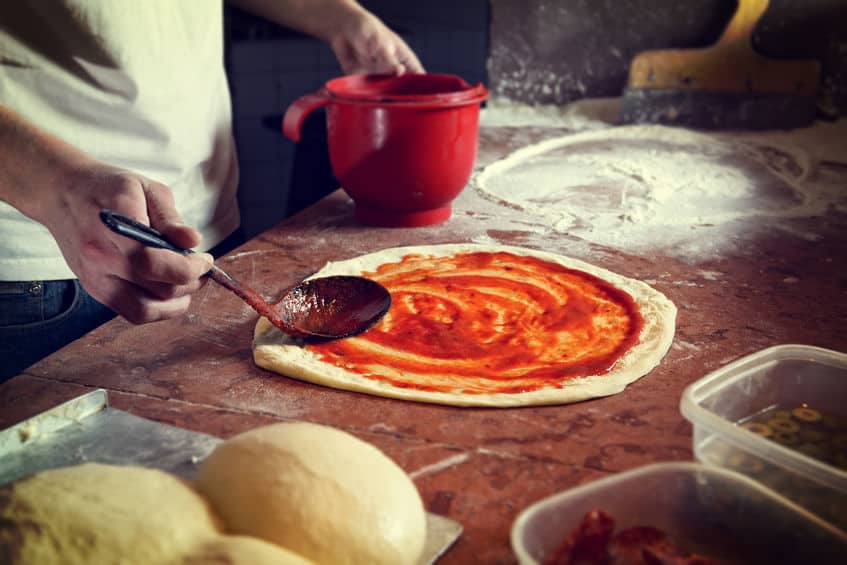 ピザを作っている写真。生地にトマトソースを塗っている