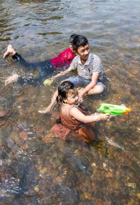 水鉄砲を構える少女、少年2人が川に浸かっている