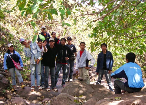 森の中で十数人のラオス人男子学生があいさつをしている写真