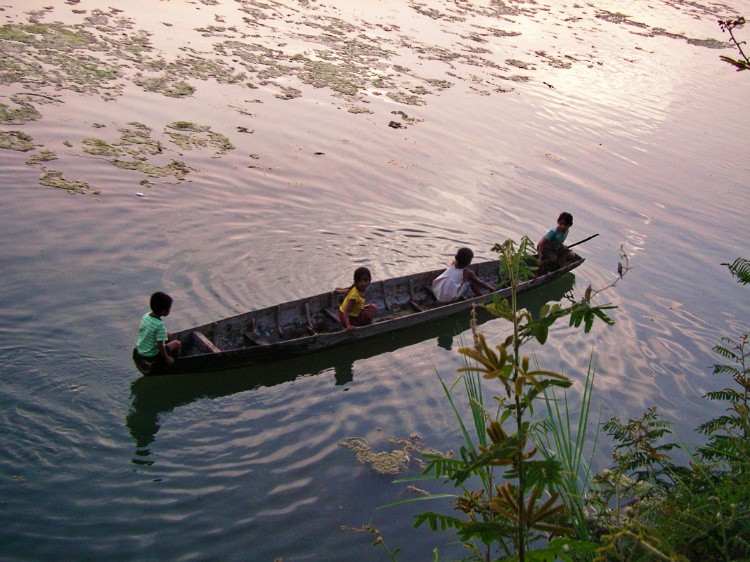 夕陽に輝く水面を４人の子どもが乗ったボートが進んでいる