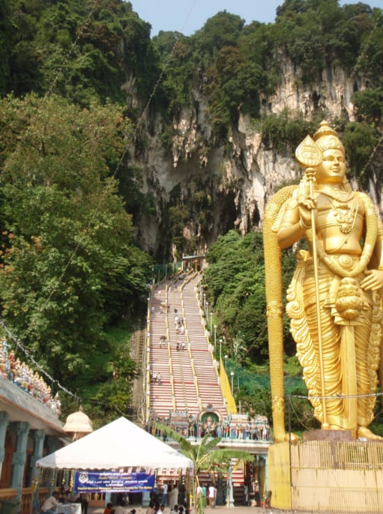 金色の巨大なヒンドゥーの像と、長い階段を上る人達。洞窟の入り口が見える
